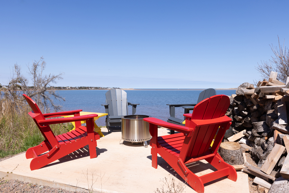 Red Adirondack chairs and fire pit overlooking St. Peter's Bay at Dune Vista Cottage, Morell PEI
